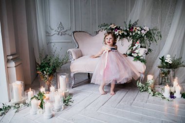 Çiçekler ve mumlarla süslenmiş beyaz bir stüdyo odasında pembe güzel elbiseler içinde güzel mutlu küçük bir kız.