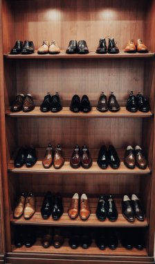 Elbise ve aksesuar dükkanında raflar. Raflarda şık erkek ayakkabıları var. Bir sürü klasik ayakkabı ve bot. Kahverengi tonlama. Mağazada güzel deri adam ayakkabıları sergileniyor.