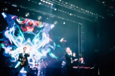 Parlak spot ışıklarının kırmızı mavi ışıklarıyla sahnede şarkı söyleyen şarkıcı ve rock grubunun bulanık renkli fotoğrafı