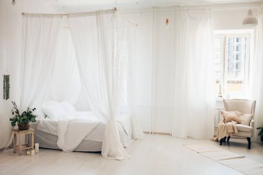 Minimalist İskandinav tarzı bir yatak odasında rahat bir yatak odası, örtülü yatak, battaniye yastıkları, bitki. Günaydın güneşli fotoğraf.