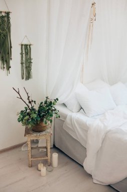 Minimalist İskandinav tarzı bir yatak odasında rahat bir yatak odası, örtülü yatak, battaniye yastıkları, bitki. Günaydın güneşli fotoğraf.