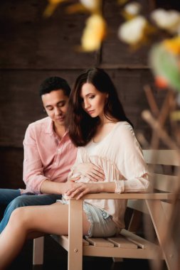 Güzel bir çift bankta oturuyor, hamile bir kadın ve kocası tahta bir arka planda.