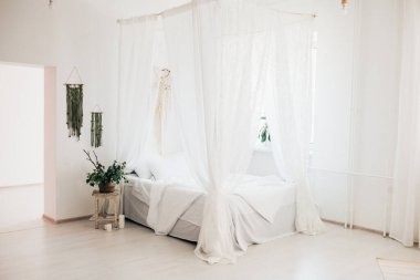 Minimalist İskandinav tarzı bir yatak odasında rahat bir yatak odası, örtülü yatak, battaniye yastıkları, bitki. Günaydın güneşli fotoğraf.