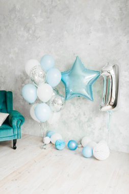 İlk doğum günü çocuğunun kutlamalarının mavi ve gümüş balonlarıyla dolu beyaz bir oda. Yıldız şeklinde ve arka planda hafif macun duvarına karşı bir numara.