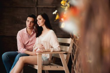 Güzel bir çift bankta oturuyor, hamile bir kadın ve kocası tahta bir arka planda.