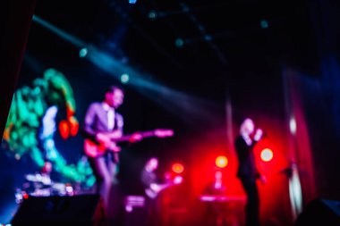 Parlak spot ışıklarının kırmızı mavi ışıklarıyla sahnede şarkı söyleyen şarkıcı ve rock grubunun bulanık renkli fotoğrafı