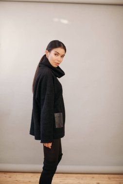 Stüdyoda, siyah elbiseli seksi bir kadın gri arka planda poz veriyor.