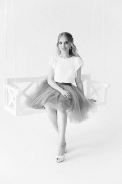 Şık etekli ve bluzlu güzel sarışın manken ahşap salıncakta oturuyor.