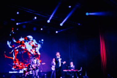 Parlak spot ışıklarının kırmızı mavi ışıklarıyla sahnede şarkı söyleyen şarkıcı ve rock grubunun bulanık renkli fotoğrafı