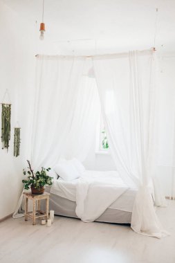 Minimalist İskandinav tarzı bir yatak odasında rahat bir yatak odası, örtülü yatak, battaniye yastıkları, bitki. Günaydın güneşli fotoğraf.