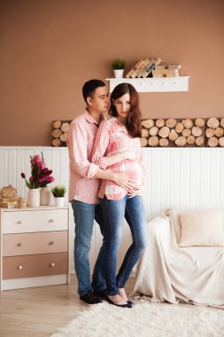 Koca, güzel hamile karısına pastel arka planda ahşap elementlerle mutlu aile çiftine sarılıyor.