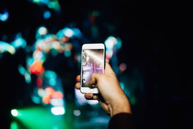 Konserdeki hayran elinde bir akıllı telefon tutuyor ve fotoğraf çekiyor ya da arka planda video çekiyor. Bir şarkıcı ve müzik grubunun bulanık performansı.