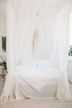 Minimalist İskandinav tarzı bir yatak odasında rahat bir yatak odası, örtülü yatak, battaniye yastıkları, bitki. Günaydın güneşli fotoğraf.