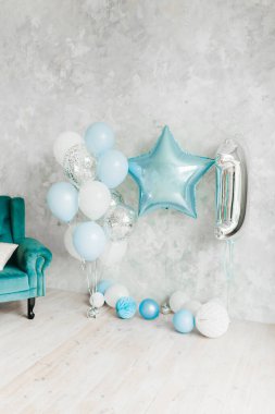 İlk doğum günü çocuğunun kutlamalarının mavi ve gümüş balonlarıyla dolu beyaz bir oda. Yıldız şeklinde ve arka planda hafif macun duvarına karşı bir numara.