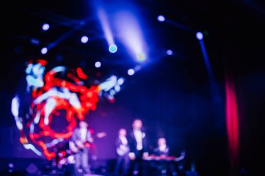 Parlak spot ışıklarının kırmızı mavi ışıklarıyla sahnede şarkı söyleyen şarkıcı ve rock grubunun bulanık renkli fotoğrafı