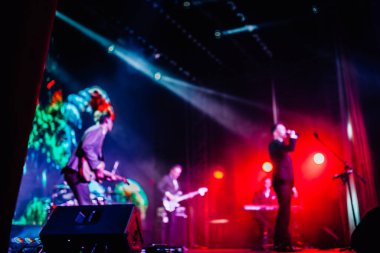 Parlak spot ışıklarının kırmızı mavi ışıklarıyla sahnede şarkı söyleyen şarkıcı ve rock grubunun bulanık renkli fotoğrafı