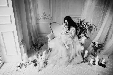 Güzel esmer kadın, annesi bir kanepede oturuyor. Sevgili kızı kollarında ve kucaklıyor. Çiçekler ve mumlarla süslenmiş parlak bir odada gülümsüyor. 