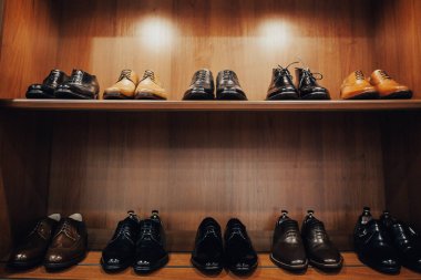 Elbise ve aksesuar dükkanında raflar. Raflarda şık erkek ayakkabıları var. Bir sürü klasik ayakkabı ve bot. Kahverengi tonlama. Mağazada güzel deri adam ayakkabıları sergileniyor.