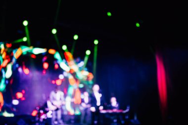 Parlak spot ışıklarının kırmızı mavi ışıklarıyla sahnede şarkı söyleyen şarkıcı ve rock grubunun bulanık renkli fotoğrafı