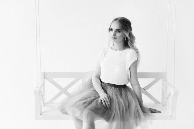 Şık etekli ve bluzlu güzel sarışın manken ahşap salıncakta oturuyor.