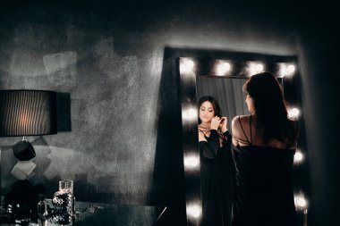 Güzel kadın büyük aynanın yanında kal. Karanlık odada ampulleri olan.