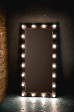 Ampullü uzun aynalar, çatı katında ahşap ve beton bir duvarın karşısında duruyor.