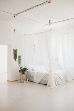 Minimalist İskandinav tarzı bir yatak odasında rahat bir yatak odası, örtülü yatak, battaniye yastıkları, bitki. Günaydın güneşli fotoğraf.