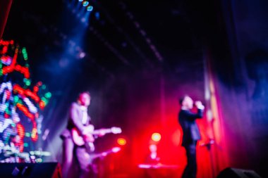 Parlak spot ışıklarının kırmızı mavi ışıklarıyla sahnede şarkı söyleyen şarkıcı ve rock grubunun bulanık renkli fotoğrafı