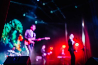 Parlak spot ışıklarının kırmızı mavi ışıklarıyla sahnede şarkı söyleyen şarkıcı ve rock grubunun bulanık renkli fotoğrafı