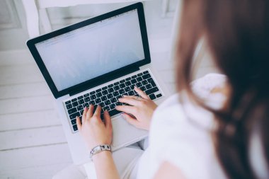 Beyaz arkaplanı olan gümüş dizüstü bilgisayarda yazan kadın.