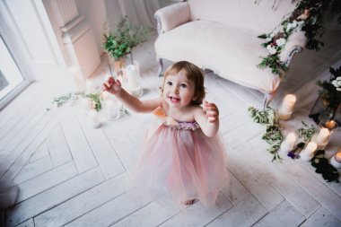 Çiçekler ve mumlarla süslenmiş beyaz bir stüdyo odasında pembe güzel elbiseler içinde güzel mutlu küçük bir kız.