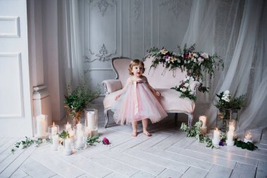 Çiçekler ve mumlarla süslenmiş beyaz bir stüdyo odasında pembe güzel elbiseler içinde güzel mutlu küçük bir kız.