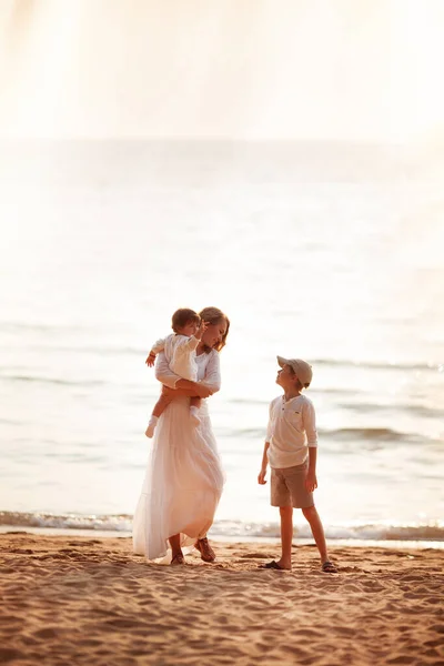 Mother with her son and daughter in her arms at sunset by the sea