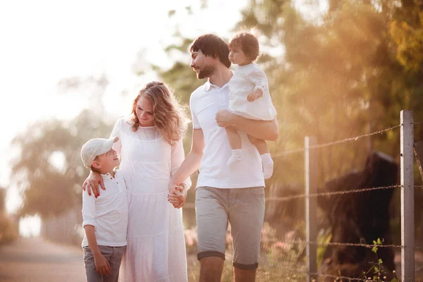 Happy family in white clothes walking together on the road at sunset