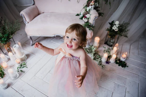 Çiçekler ve mumlarla süslenmiş beyaz bir stüdyo odasında pembe güzel elbiseler içinde güzel mutlu küçük bir kız.