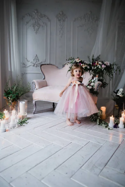 Çiçekler ve mumlarla süslenmiş beyaz bir stüdyo odasında pembe güzel elbiseler içinde güzel mutlu küçük bir kız.