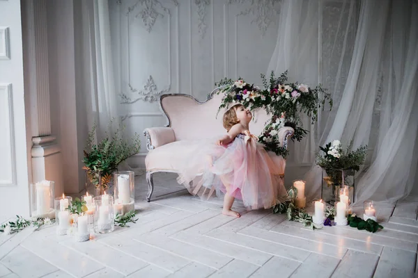 Çiçekler ve mumlarla süslenmiş beyaz bir stüdyo odasında pembe güzel elbiseler içinde güzel mutlu küçük bir kız.