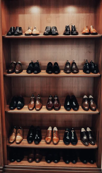Elbise ve aksesuar dükkanında raflar. Raflarda şık erkek ayakkabıları var. Bir sürü klasik ayakkabı ve bot. Kahverengi tonlama. Mağazada güzel deri adam ayakkabıları sergileniyor.
