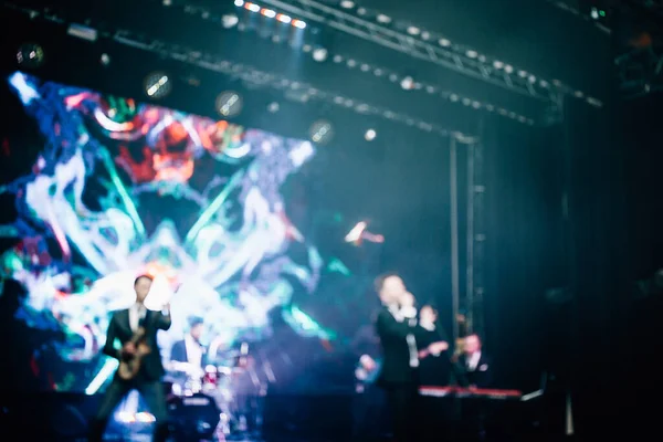 Parlak spot ışıklarının kırmızı mavi ışıklarıyla sahnede şarkı söyleyen şarkıcı ve rock grubunun bulanık renkli fotoğrafı