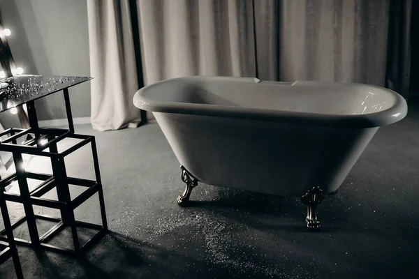 luxurious detached bath on bronze legs in a dark decorated bathroom in gray, black with a decor, a mirror, a table and curtains to the floor. photo taken at night