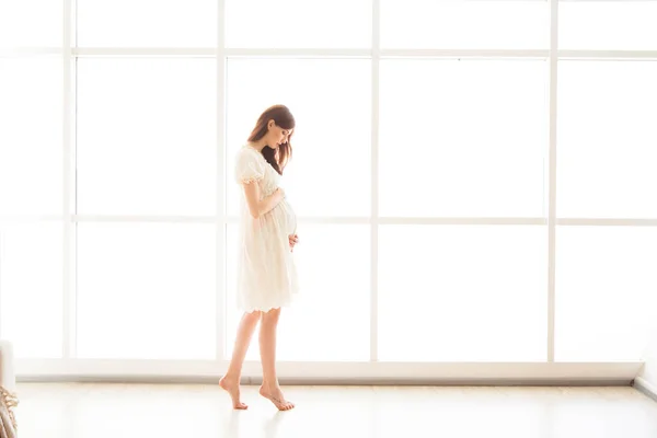 穿着鲜艳衣服的漂亮孕妇正站在一个全景窗口的后面 — 图库照片