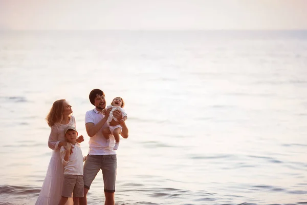 Young happy family in white clothes stands on the beach at sunset