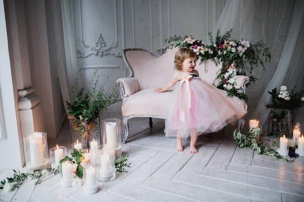 Çiçekler ve mumlarla süslenmiş beyaz bir stüdyo odasında pembe güzel elbiseler içinde güzel mutlu küçük bir kız.
