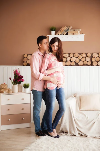 Koca, güzel hamile karısına pastel arka planda ahşap elementlerle mutlu aile çiftine sarılıyor.