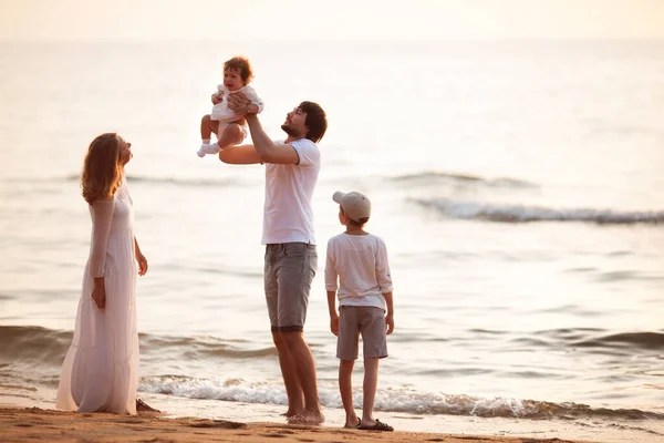 Young happy family in white clothes stands on the beach at sunset
