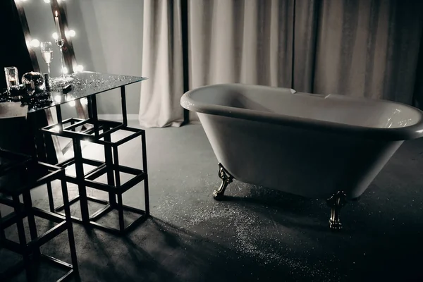 luxurious detached bath on bronze legs in a dark decorated bathroom in gray, black with a decor, a mirror, a table and curtains to the floor. photo taken at night