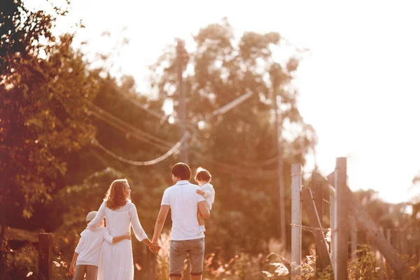 Happy family in white clothes walking together on the road at sunset