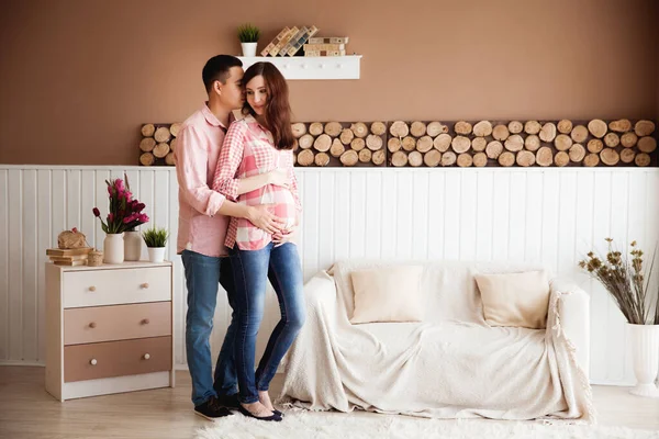 Koca, güzel hamile karısına pastel arka planda ahşap elementlerle mutlu aile çiftine sarılıyor.