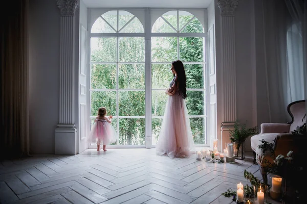 Anne ve kızı büyük beyaz bir pencerenin yanında güzel pembe şifon elbiseler içinde klasik dekore edilmiş bir odada duruyorlar.