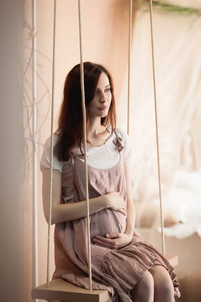 穿着粉色衣服坐在秋千上的孕妇 — 图库照片